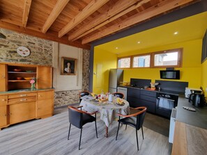 A dining area with a table set for four, a stone wall, and a yellow wall with windows. - Welcoming gîte, pets allowed - 5 guests (Doizieux)