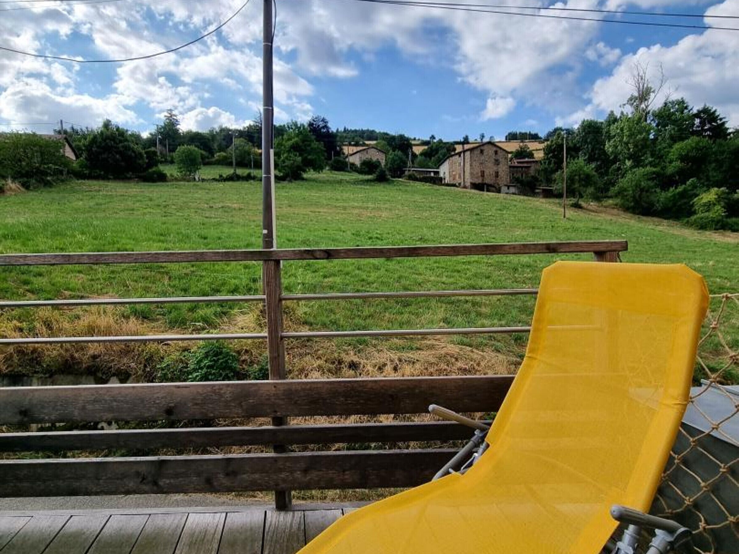A yellow chair on a wooden deck overlooking a grassy field with a clear sky.
