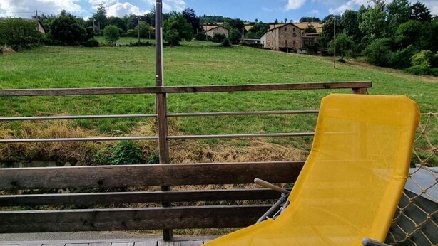 Ein gelber Stuhl auf einer Holzdielen-Terrasse mit Blick auf ein grünes Feld und einen klaren Himmel.