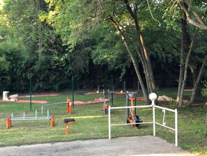 Ein Trainingsbereich im Freien mit verschiedenen Fitnessgeräten, umgeben von Bäumen und einem eingezäunten Bereich.