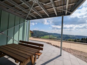Ein überdachter Sitzbereich mit einer Bank und Blick auf eine grüne Landschaft.