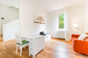 A modern living room with a white desk, a green cushioned chair, a red sofa, and a window with curtains. - URNEST Colli - 1 bedroom apartment in the first hills surrounding Bologna (Bologna)