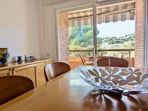 A dining area with a table, chairs, and a view of a balcony with a brick wall and greenery. - Apartment with pool, pets OK - 6 guests (Tossa de Mar)