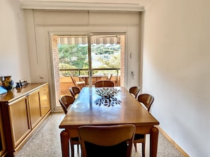 A dining area with a table and chairs, a view through a glass door, and a kitchen counter. - Apartment with pool, pets OK - 6 guests (Tossa de Mar)