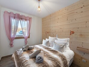 Ein Schlafzimmer mit Holzwand, einem Bett mit weißer Bettwäsche und einem Fenster mit rosa Vorhängen.