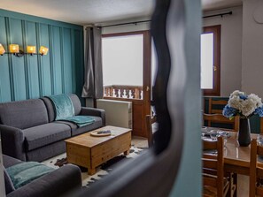 Ein Wohnzimmer mit einer Couch, einem Couchtisch und einem Essbereich mit Stühlen und einem Blumenstrauß.