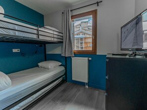 A small room with a bunk bed, a desk with a computer, a window with a view of buildings, and a radiator. - Cozy apartment, panoramic view - 8 guests (Belle Plagne)