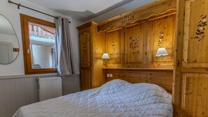 A bedroom with a large bed, wooden wardrobe, two wall-mounted lamps, and a window with curtains. - Cozy apartment, panoramic view - 8 guests (Belle Plagne)