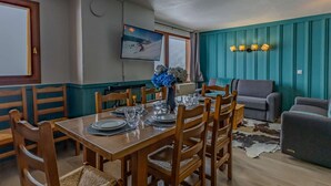 A dining area with a wooden table set for six, surrounded by chairs, and a living area with a sofa and a cowhide rug. - Cozy apartment, panoramic view - 8 guests (Belle Plagne)