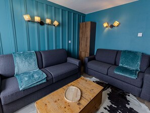 Ein modernes Wohnzimmer mit zwei dunklen Sofas, einem Holztisch und teal-farbenen Wänden.