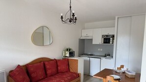 Um espaço compacto com sofá, mesa de jantar, área de cozinha e espelho.