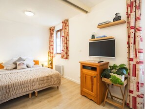 A bedroom with a bed, a TV on a wooden stand, a shelf with books, and a window with curtains. - Cozy apartment - 4 guests (Vignec)