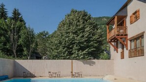 Uma piscina com espreguiçadeiras, um deque de madeira e um edifício com varanda.
