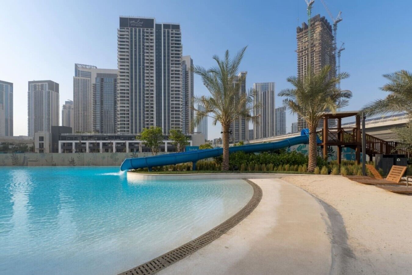 Une piscine avec un toboggan bleu, des palmiers et, en arrière-plan, des immeubles de grande hauteur.