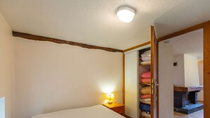 Et soveværelse med seng, sengetlampe, træsenggavl, skab med håndklæder og pejs.