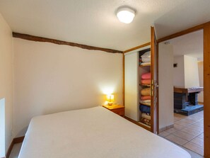 Ein Schlafzimmer mit Bett, Nachttischlampe, Holz-Kopfteil, Kleiderschrank mit Handtüchern und Kamin.