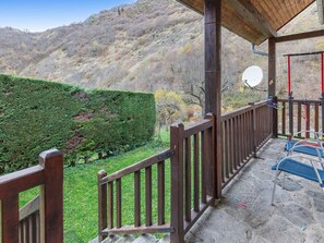 Ein überdachter Außenbereich mit Hollerkerbung, Steinboden und Blick auf eine grüne Hecke und Hügel.