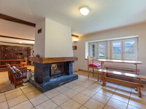 Ein Wohnzimmer mit Kamin, Holzmöbeln, einem Fenster mit Blick und einem Fliesenboden.
