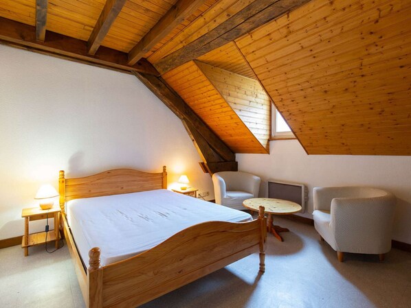 A bedroom with a wooden ceiling, a bed, a chair, a small table, and a lamp.