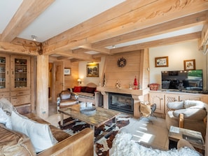 A cozy living room with wooden beams, a fireplace, leather sofas, and a television. - Chalet central village mountain view - 11 guests (La Clusaz)