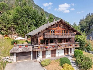 A two-story wooden chalet with a balcony, surrounded by forested mountains. - Chalet central village mountain view - 11 guests (La Clusaz)