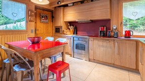 Um interior de madeira com uma área de cozinha, incluindo uma mesa vermelha, cadeiras, um fogão e uma cafeteira.