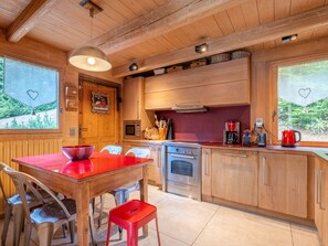 A wooden interior with a kitchen area featuring a red table, chairs, a stove, and a coffee maker. - Chalet central village mountain view - 11 guests (La Clusaz)