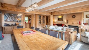 Um quarto espaçoso com uma grande mesa de jantar de madeira, uma lareira e um espaço de estar acolhedor.