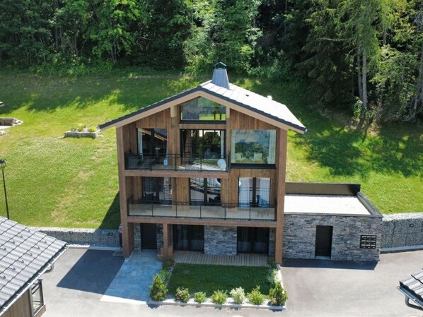 Ein modernes, zweistöckiges Haus mit Balkon, umgeben von einem gepflegten Rasen und Bäumen.