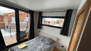 A bedroom with a bed, a window with curtains, a wooden floor, and a view of the outside. - Prestige chalet, mountain view - 10 guests (La Plagne Montalbert)