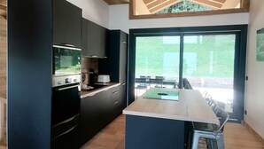 A modern kitchen with a central island, built-in appliances, and a large sliding glass door leading to an outdoor area. - Prestige chalet, mountain view - 10 guests (La Plagne Montalbert)