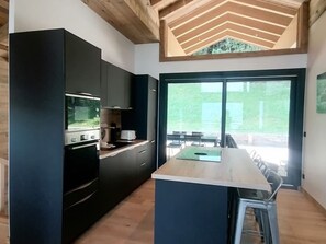 A modern kitchen with a central island, built-in appliances, and a large sliding glass door leading to an outdoor area. - Prestige chalet, mountain view - 10 guests (La Plagne Montalbert)