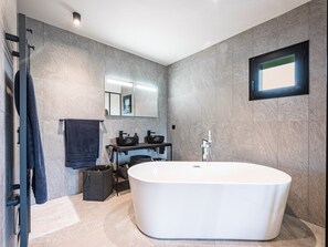 Ein modernes Badezimmer mit einer freistehenden Badewanne, einem Spiegel und einem Fenster.