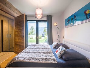 Ein Schlafzimmer mit Bett, Nachttisch, Lampe, Gemälde und Blick ins Freie.