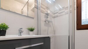 Ein modernes Badezimmer mit Duschkabine aus Glas, einem weißen Waschbecken und zwei Topfpflanzen sowie einem großen Spiegel.