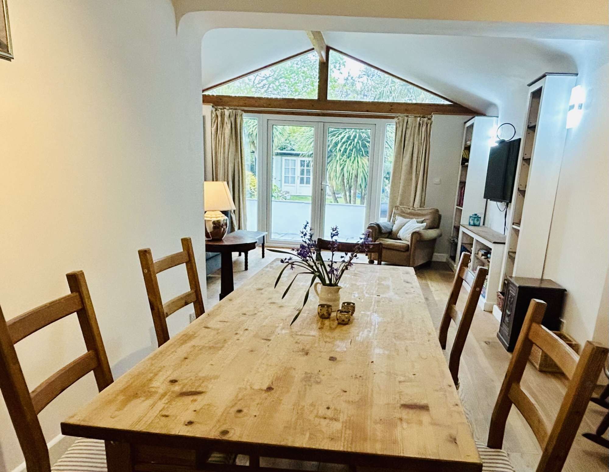 A dining area with a wooden table, chairs, and a vase with flowers.