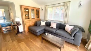 A living room with a sectional sofa, a wooden cabinet, a dining table with chairs, and a window with blinds. - Near the River and Marinas, quick walk to town Large Garden and off street parking for 3 cars (Lymington)