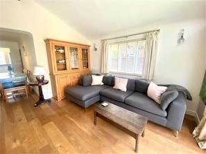 A living room with a sectional sofa, a wooden cabinet, a dining table with chairs, and a window with blinds. - Near the River and Marinas, quick walk to town Large Garden and off street parking for 3 cars (Lymington)