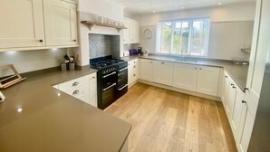 A modern kitchen with white cabinetry, a central island, and a window with blinds. - Near the River and Marinas, quick walk to town Large Garden and off street parking for 3 cars (Lymington)