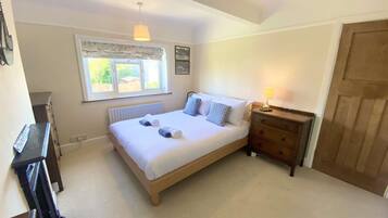A bedroom with a bed, a dresser, a radiator, a window, and a door.
