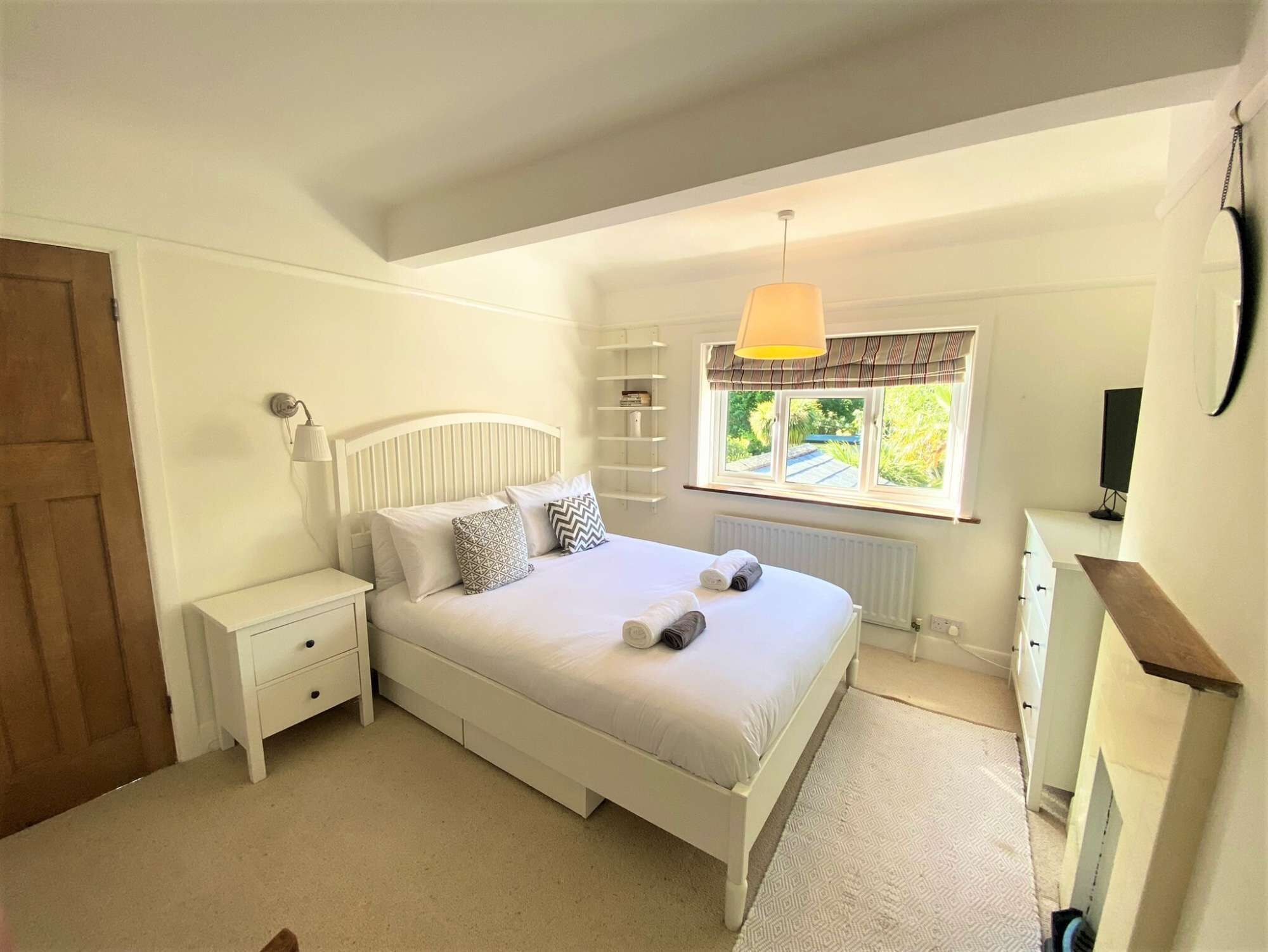 A bedroom with a bed, nightstands, a window with curtains, a radiator, and a television on a stand.