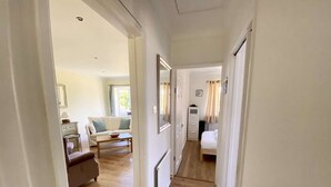A narrow hallway with a sofa, a small table, and a bed in the distance. - Daisy Cottage by NewFo dot Rest (Lymington)