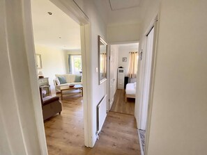 A narrow hallway with a sofa, a small table, and a bed in the distance. - Daisy Cottage by NewFo dot Rest (Lymington)