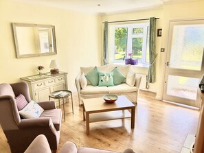 A living room with a sofa, armchair, coffee table, and a dresser with a mirror. - Daisy Cottage by NewFo dot Rest (Lymington)