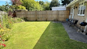 A backyard with a wooden fence, a barbecue grill, and outdoor furniture. - Daisy Cottage by NewFo dot Rest (Lymington)