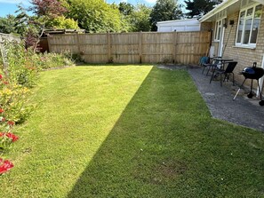 A backyard with a wooden fence, a barbecue grill, and outdoor furniture. - Daisy Cottage by NewFo dot Rest (Lymington)