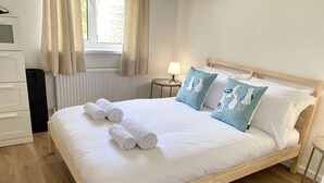 A neatly made bed with rolled towels, a wooden headboard, and a view of the outdoors through a window. - Daisy Cottage by NewFo dot Rest (Lymington)