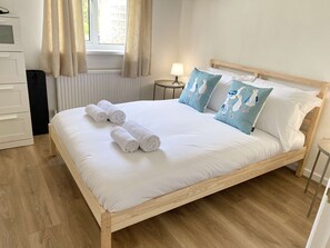 A neatly made bed with rolled towels, a wooden headboard, and a view of the outdoors through a window. - Daisy Cottage by NewFo dot Rest (Lymington)