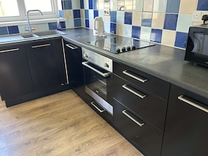 A modern kitchen with black cabinets, stainless steel appliances, and a blue and white tiled backsplash. - Daisy Cottage by NewFo dot Rest (Lymington)