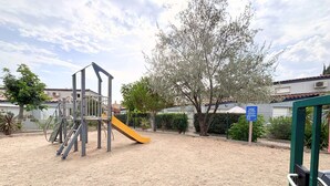 Un parc infantil amb tobogan i elements per a escalar, envoltat de sorra i arbres.
